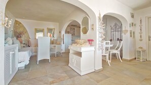Ampla sala de estar com teto alto, paredes brancas e arco de pedra. Há uma mesa de jantar com cadeiras, um sofá branco e um armário branco.
