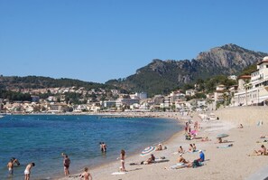 Une plage où l’on voit des gens se prélasser au soleil et nager, des bâtiments le long du rivage et une montagne en arrière-plan.