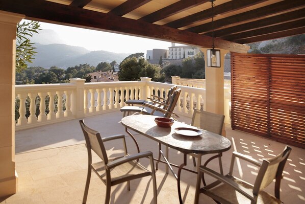 Un balcon avec une table et des chaises, une clôture en bois et une vue sur les montagnes et les bâtiments.