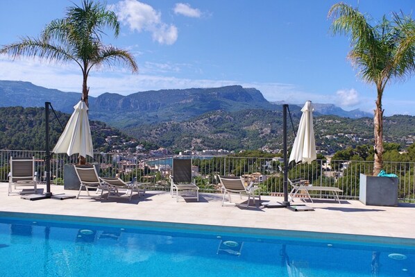 A poolside area with lounge chairs and umbrellas, overlooking a mountainous landscape.