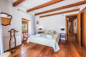 Une chambre avec un plafond en bois, un lit recouvert d’une couverture à rayures, une chaise, une table de chevet avec une lampe et une fenêtre avec des rideaux.