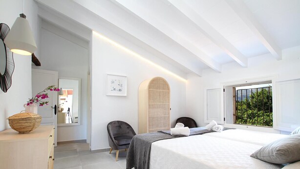 A modern bedroom with a large bed, a chair, a desk, and a window with a view of greenery. - H2904 Finca Creva with pool for 10 people in Pollenca (Pollenca)