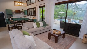 Ein großzügiger Wohnbereich mit einer Couch, Couchtisch und Blick auf Pool und Garten durch große Schiebetüren.