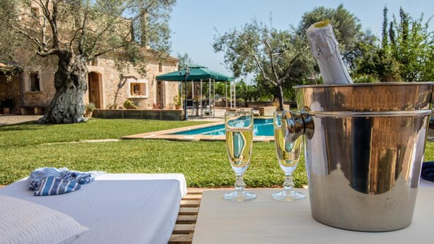 Zona piscina con un letto, un secchio con bicchieri da champagne e un edificio in pietra sullo sfondo.