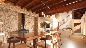 A rustic interior with a stone wall, wooden dining table, woven chairs, and a staircase leading to another level. - H2910 Finca Bennassar Pollensa (Pollenca)
