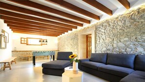 Uma sala de estar moderna com parede de pedra, vigas de madeira, um sofá, uma mesa de centro e uma mesa de futebol.