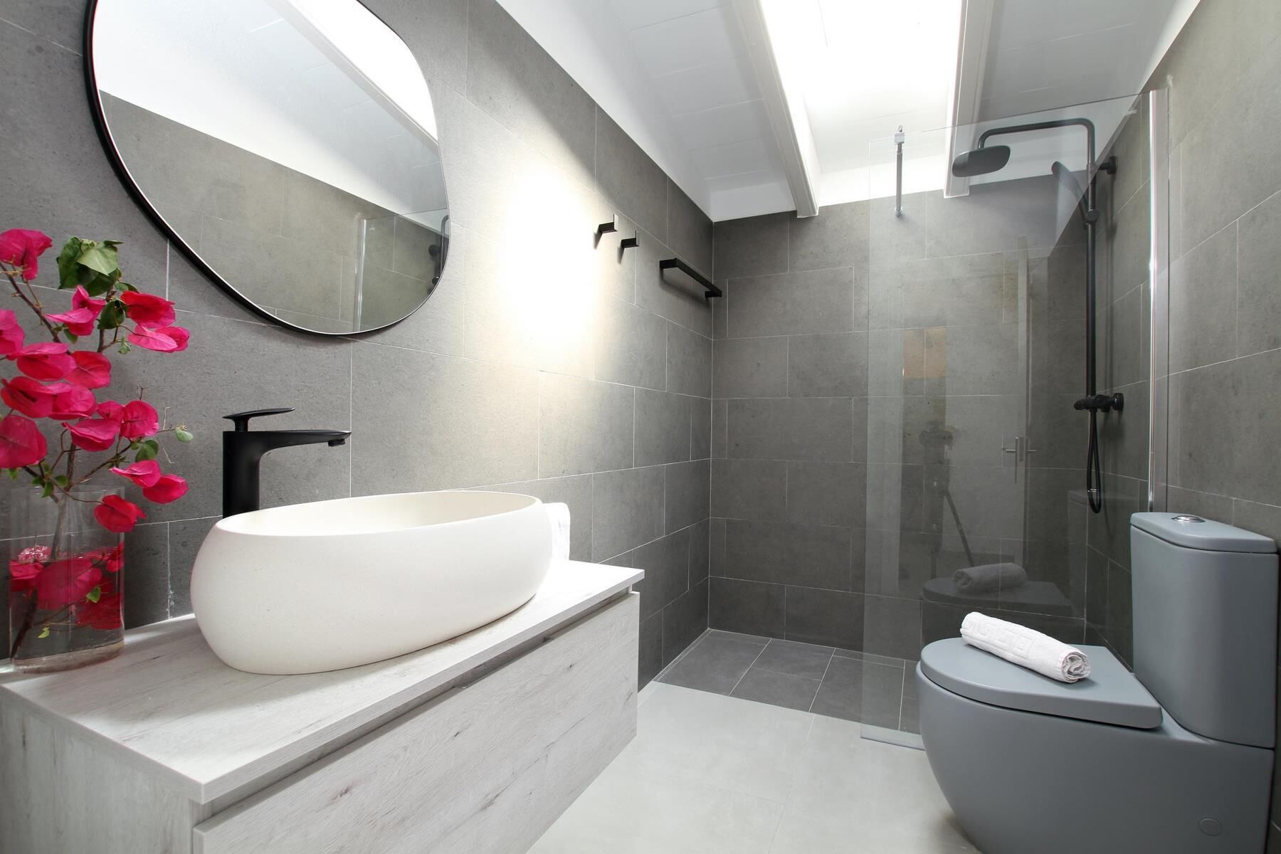 Une salle de bain moderne avec un grand lavabo sur pied blanc, des toilettes et une douche séparée par une paroi de verre.