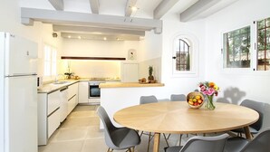 Een moderne keuken met witte kasten, een inbouwoven en een eethoek met een ronde houten tafel en grijze stoelen.