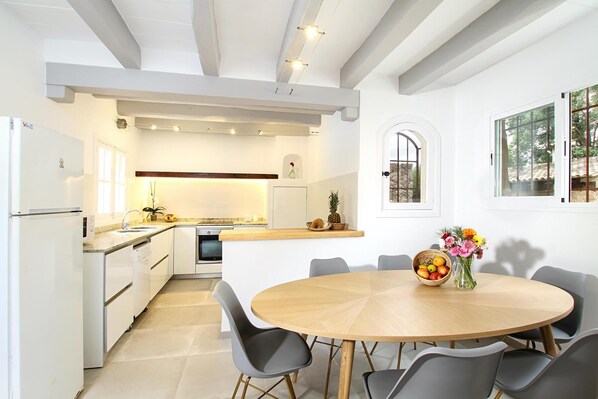 A modern kitchen with white cabinetry, a built-in oven, and a dining area with a round wooden table and grey chairs.
