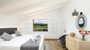 Een slaapkamer met een groot bed, een raam met uitzicht op groen, een stoel, een dressoir en een spiegel.