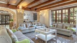 Ein geräumiges Wohnzimmer mit hoher Decke, Holzbalken und großen Fenstern. Zwei Sofas und ein Couchtisch sind vorhanden.