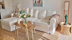 Ein modernes Wohnzimmer mit einem weißen Sofa, einem kleinen Holztisch mit Blumenvase und einem Gemälde an der Wand.