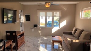 A living room with a ceiling fan, a TV mounted on the wall, a sofa, a coffee table, and a TV stand. - Very clean1 bedroom sleeps 4. Close to shopping and beach. Neighborhood setting  (Tanki Flip)