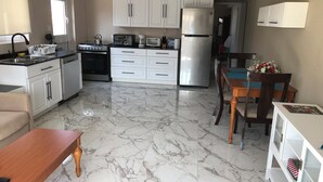 A compact kitchen with white cabinets, a refrigerator, a stove, and a dining area with a wooden table and chairs. - Very clean1 bedroom sleeps 4. Close to shopping and beach. Neighborhood setting  (Tanki Flip)