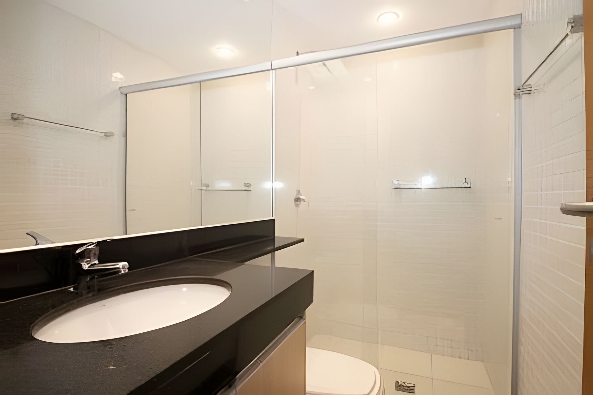 A modern bathroom with a black countertop, a white sink, and a glass shower enclosure.