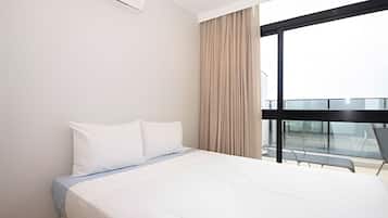 A modern hotel room with a large bed, a window with a view of a building, and a balcony with glass railings.