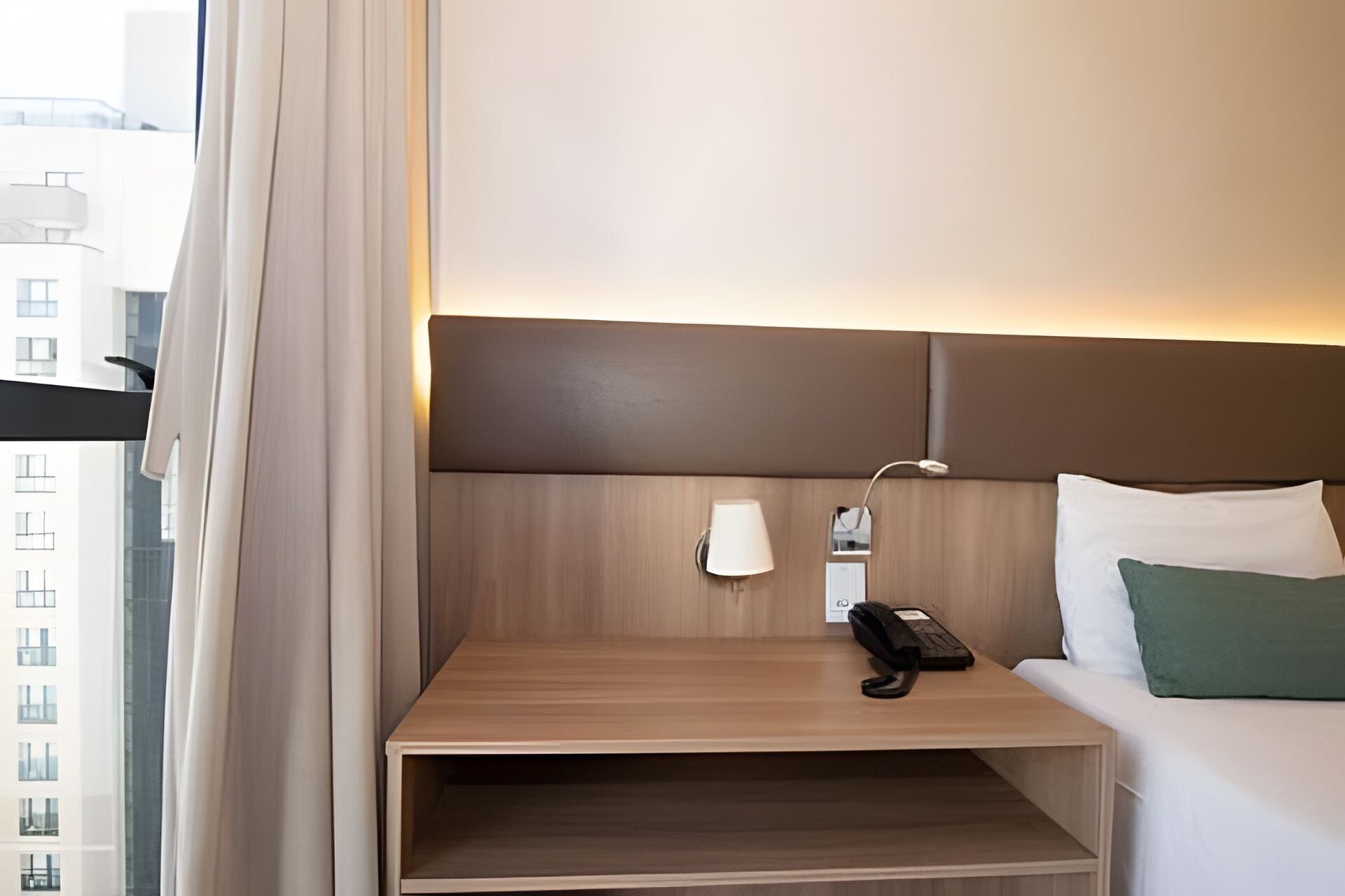 Et hotelværelse med seng, sengetårn, telefon og en lille træhylde.