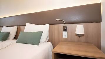 Una habitación de hotel con una cama, almohadas, una mesita de noche y una lámpara de pared.