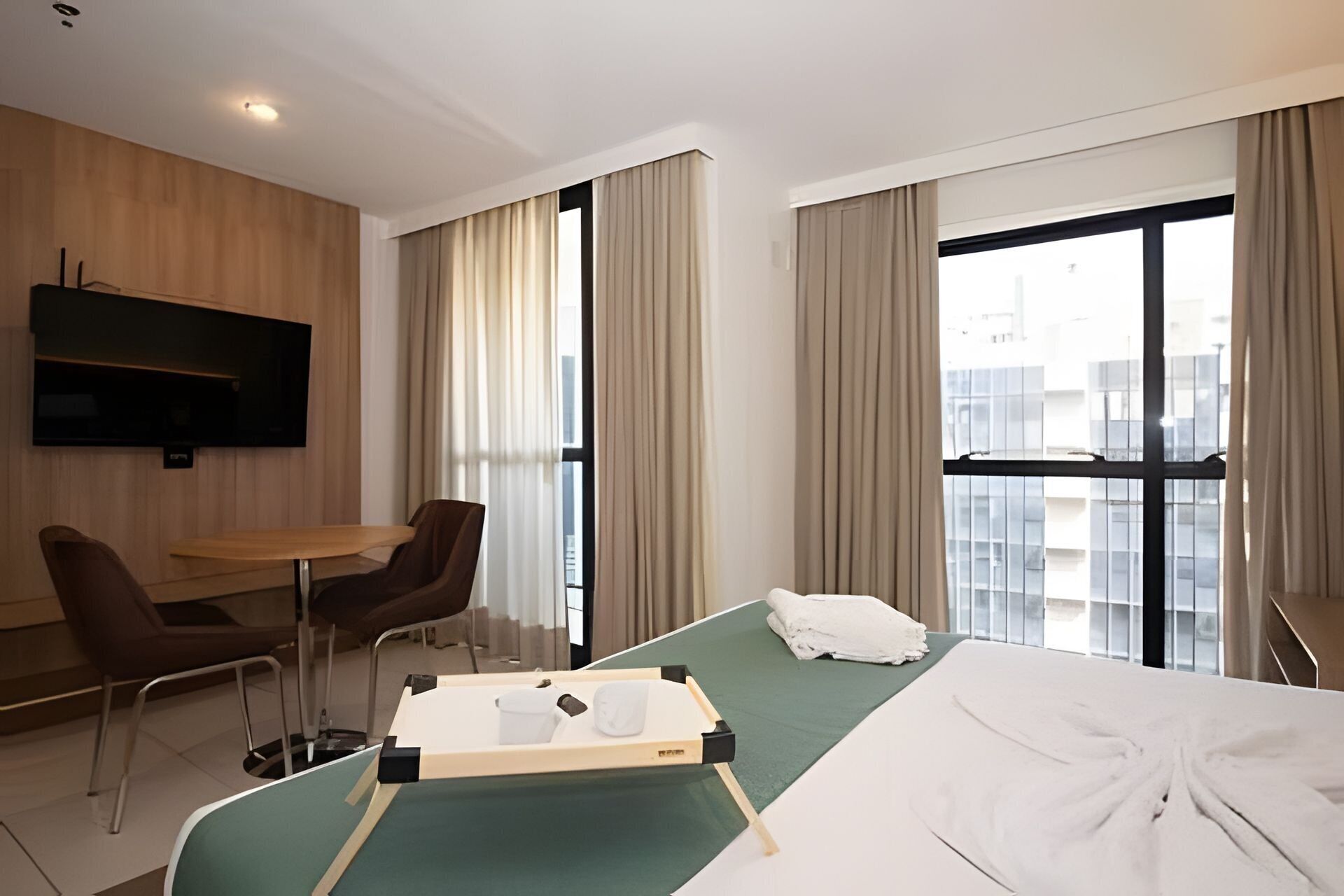 A hotel room with a bed, a desk, a chair, a television, and large windows.