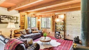A cozy cabin interior with a wooden ceiling, a leather sofa, a round coffee table, and a plaid rug.