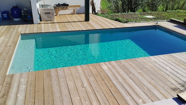 Una piscina rectangular con agua azul cristalina, rodeada por una terraza de madera.