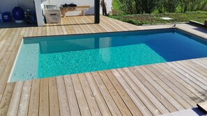 Ein rechteckiger Pool mit klarem, blauem Wasser, umgeben von einer Holzterrasse.