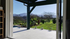 Vista desde un porche cubierto con piscina, rodeado de follaje y montañas a lo lejos.