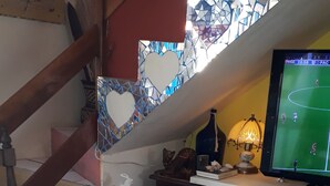 A dining area with a table set for two, featuring a bowl of fruit, a remote control, and a decorative lamp. - Casa Hostel Mosaicos DyA (Florianópolis)