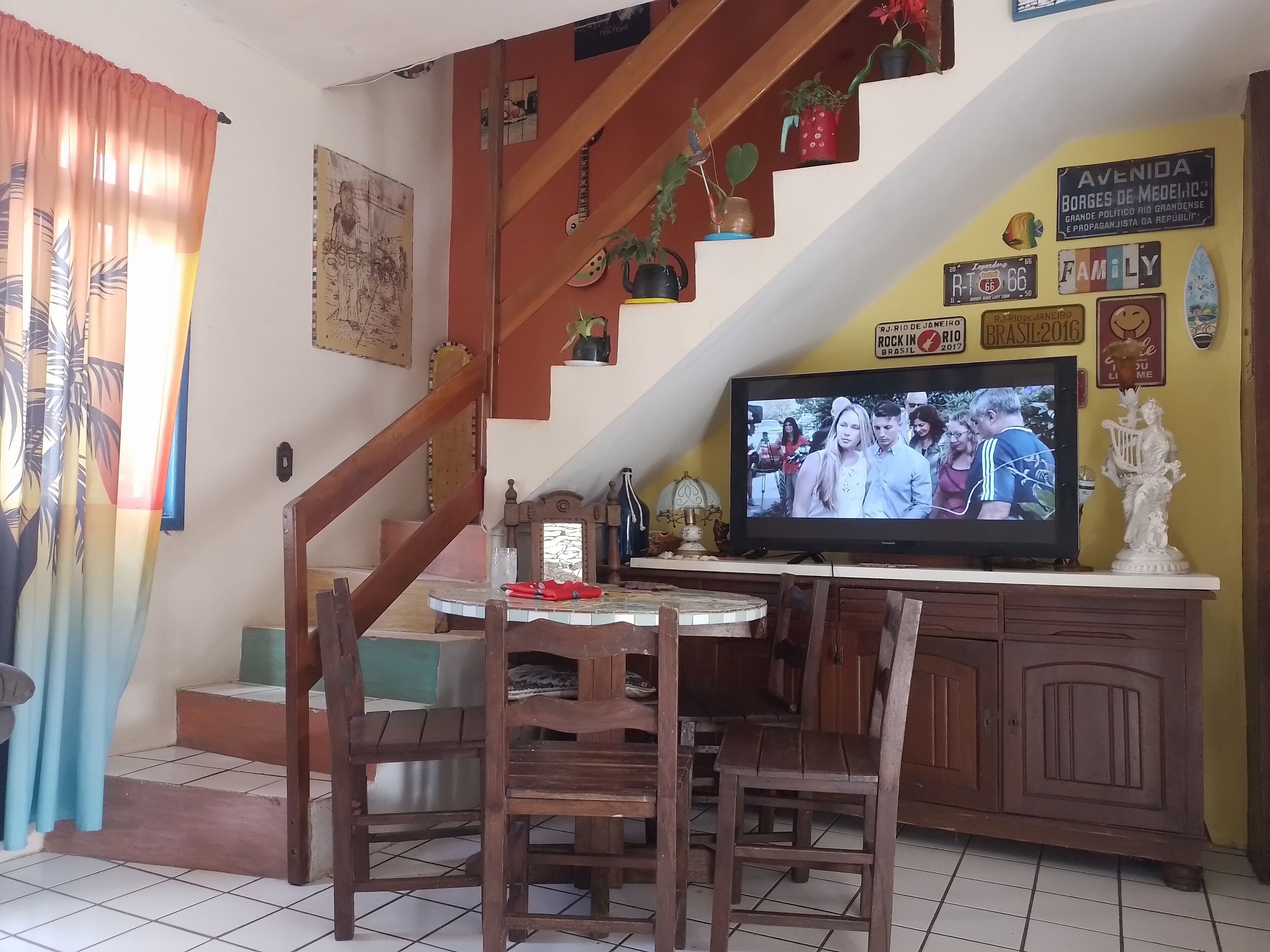 Un salon chaleureux avec un escalier en bois, une table à manger avec des chaises, un téléviseur et divers éléments de décoration, notamment une horloge et un panneau.