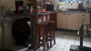 A kitchen with a tiled floor, a wooden cabinet, a microwave, and a fan. - Casa Hostel Mosaicos DyA (Florianópolis)