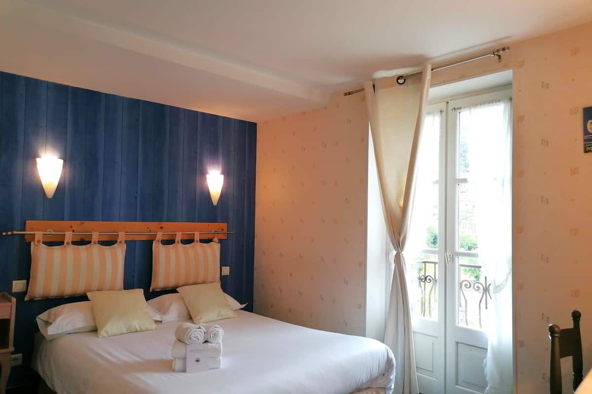A hotel room with a bed, two wall-mounted lights, a window with curtains, and a balcony view.