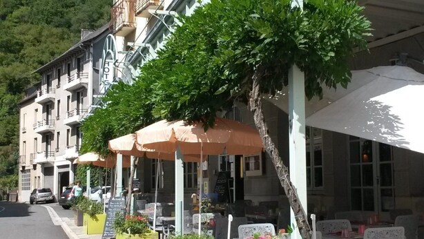 A building with a 'Logis' sign, outdoor seating with umbrellas, and a restaurant sign. - Hôtel Aux Armes d'Estaing (Estaing)