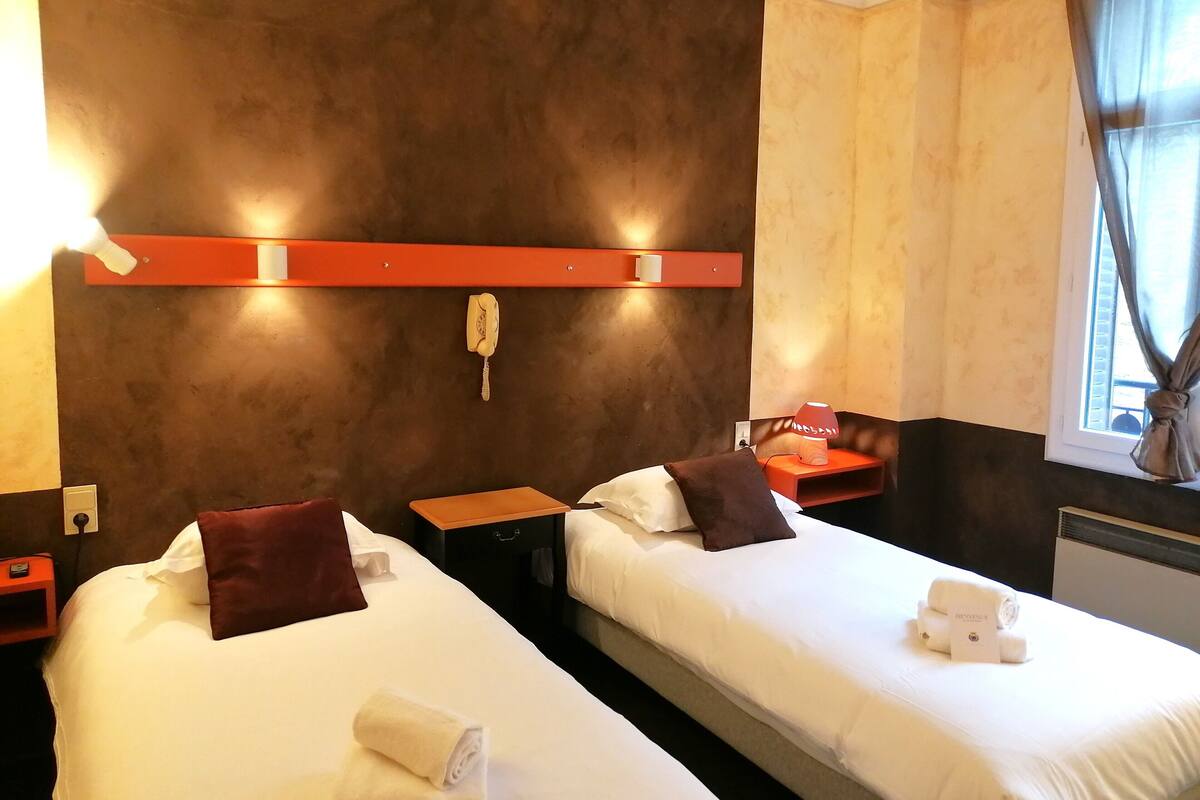 A hotel room with two beds, a telephone, a nightstand, and a window with curtains.