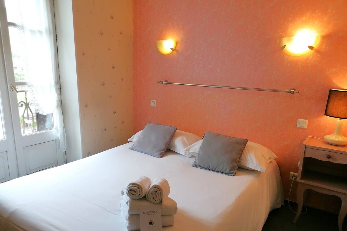 A neatly made bed with pillows, a bedside table with a lamp, and a window with curtains.