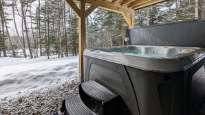 Un jacuzzi bajo una pérgola de madera con un bosque nevado de fondo.