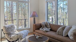 Una sala de estar acogedora con ventanas amplias, un sofá, un sillón y una lámpara.