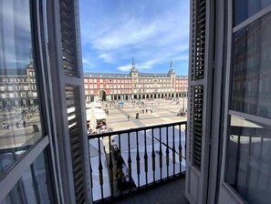 A view from a balcony with a railing, overlooking a plaza with a large building in the background. - Apartamento/ Madrid Centro/ Vista a la Plaza Mayor (Madrid)