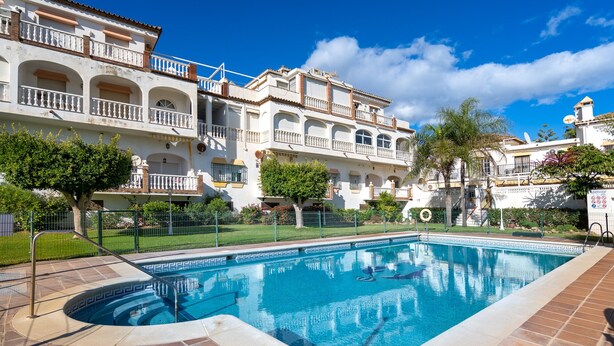 A swimming pool with a tiled deck, surrounded by a fence and trees. - CALLE COMPETA 11 (LAS LAGUNAS DE MIJAS,)