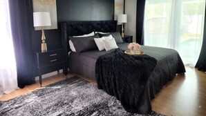 Une chambre moderne aux couleurs sombres, avec un grand lit doté d’une tête de lit capitonnée, deux tables de chevet avec des lampes et un plaid noir et moelleux sur le lit.