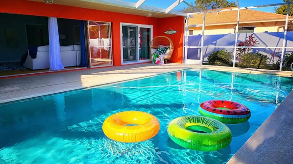 A swimming pool with three inflatable rings, a covered patio area, and a red building with glass doors.