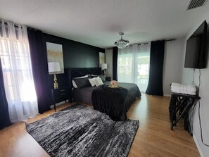 A bedroom with two beds, a large rug, a bedside table with a lamp, and a TV on the wall.
