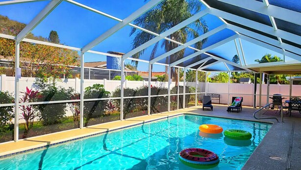 Une piscine dotée d’une enceinte en verre, entourée de plantes et agrémentée d’un espace patio.