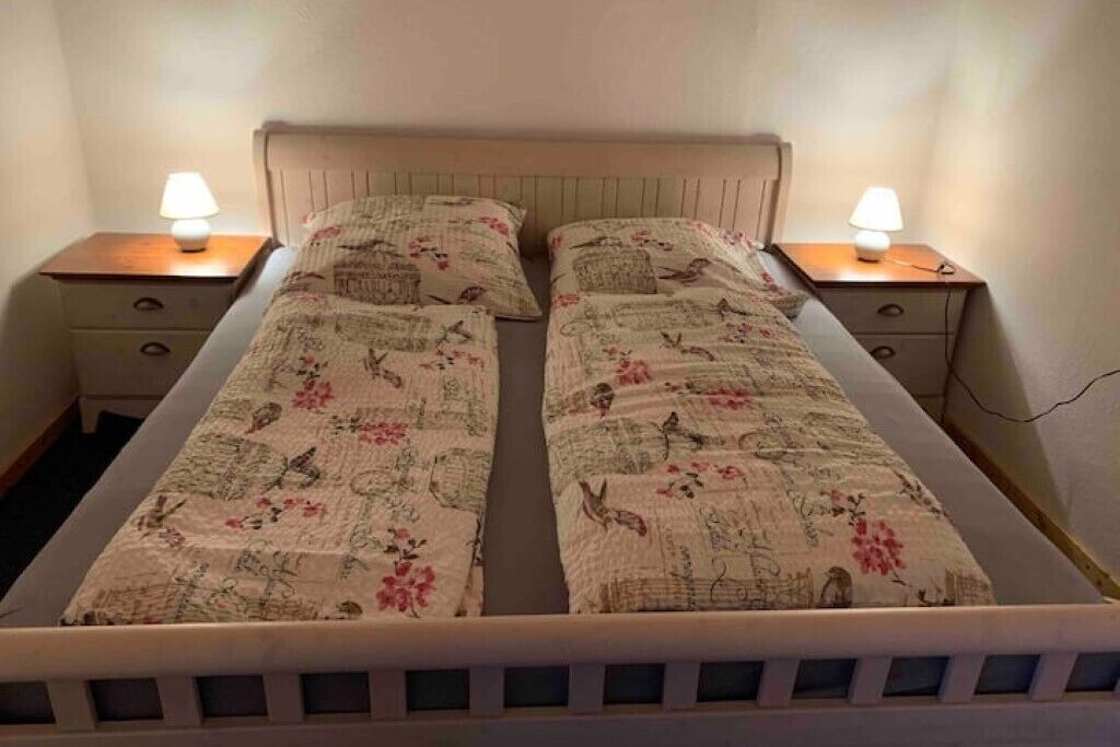 A double bed with floral bedding, two bedside tables with lamps, and a wooden headboard.