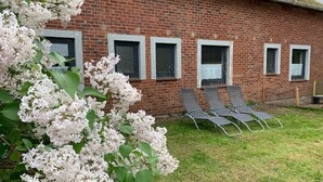 Un bâtiment en briques avec quatre fenêtres, une pelouse verdoyante et trois chaises longues.