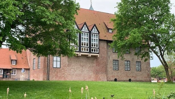 Un bâtiment historique doté d’une tour imposante et de nombreuses fenêtres, entouré d’une pelouse bien entretenue et d’arbres.