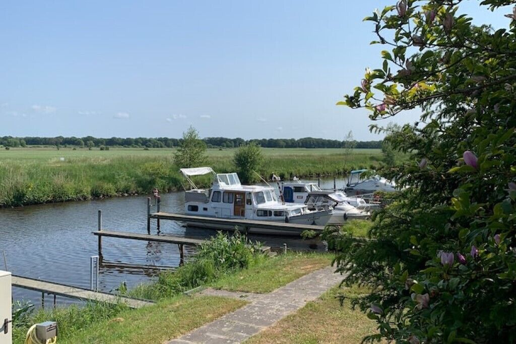 A canal with a houseboat docked at a wooden pier.
