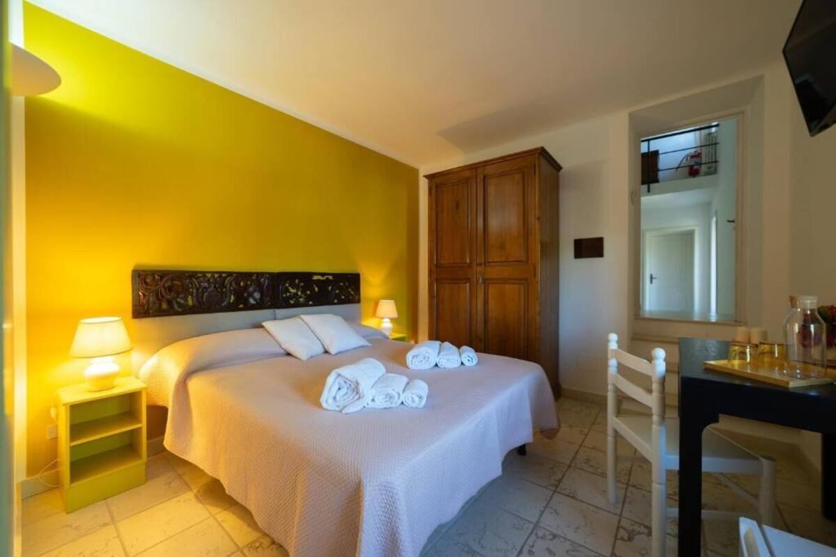 Een hotelkamer met een bed, een houten garderobe, een bureau met stoel en een spiegel.