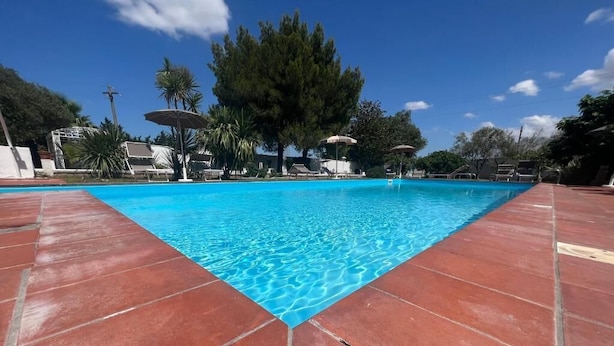 Una piscina con agua cristalina azul, rodeada de baldosas rojas y con sombrillas.