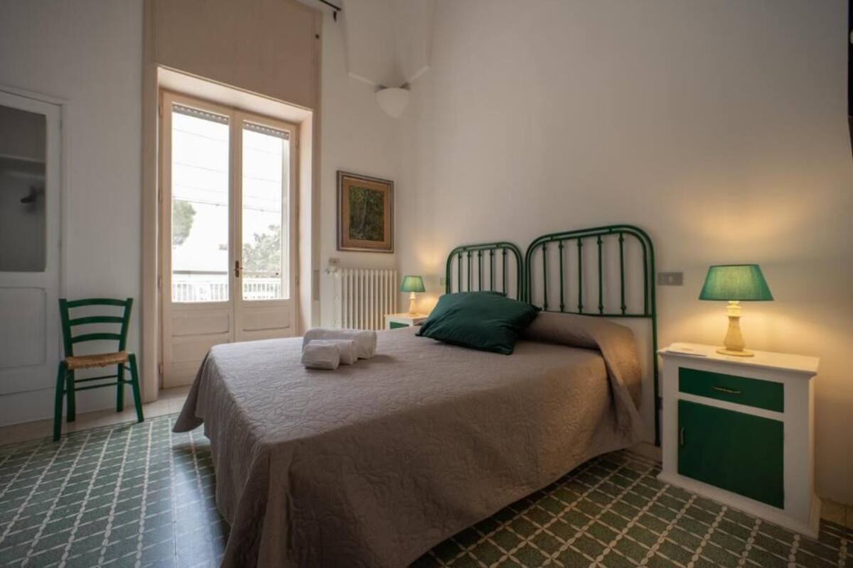 Een slaapkamer met een bed, twee nachtkastjes met lampen, een stoel, een radiator en een deur naar een balkon.