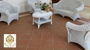 Un amplio espacio al aire libre con mobiliario de mimbre blanco, piso de baldosas y una escalera que sube a un nivel superior.